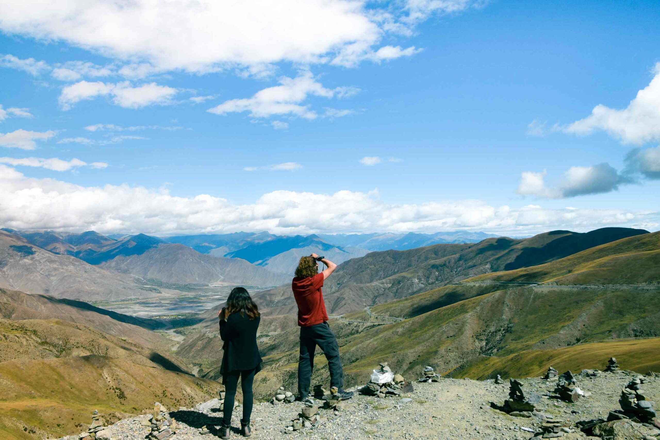 Altitude Sickness in Tibet: Two travelers taking photos and looking out over the scenic mountain landscape from Kamba La Pass in Tibet.